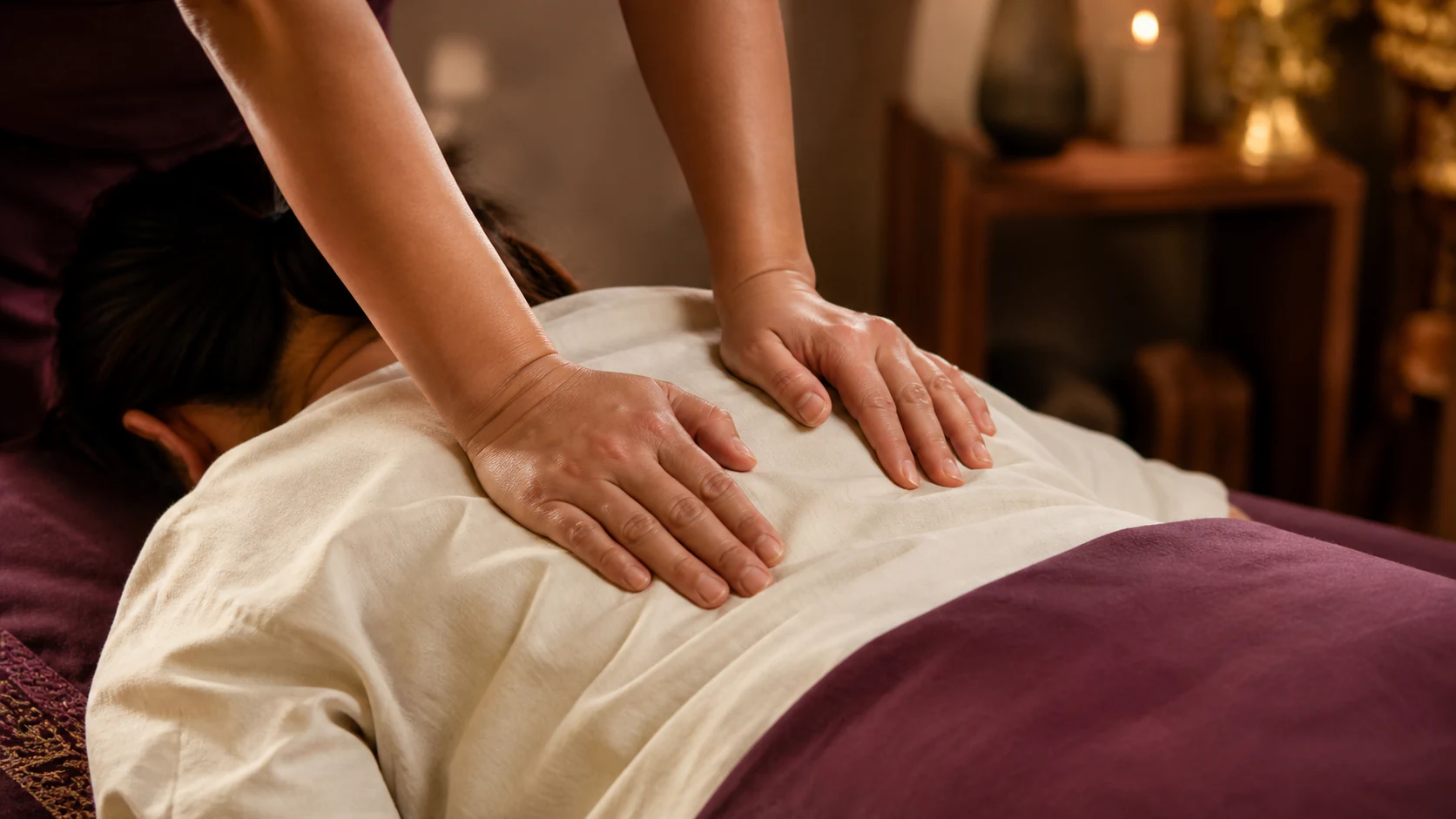 Therapist applying rhythmic palm pressure over a clothed back during traditional Thai massage